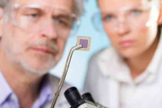 Focused senior engineer holding and showing the micro chip to his student. Lens focus on the chip.