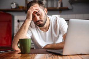 Bored young man using laptop computer while sitting at the kitchen table
