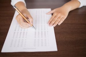 Close-up of female hand holding pen and marking answers in questionnaire form. Student doing examination test