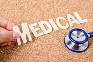 Hand arrange wood letters as medical word with stethoscope on wooden background.