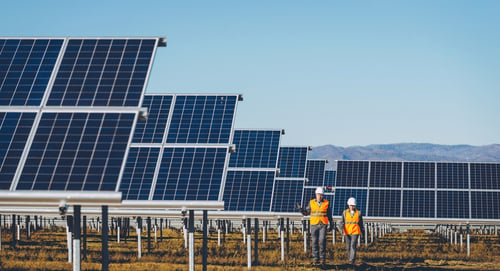 Two men wearing protective gear, monitoring solar panels