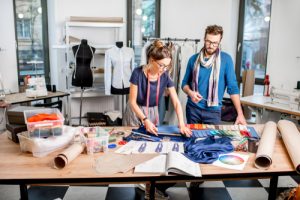 Woman trying to cut fabric on a table while a man watches over her