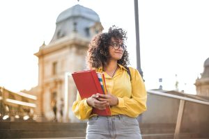 A college student holding books and papers outside
