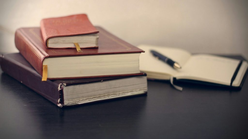 Three books neatly arranged on a table, accompanied by a pen and notebook