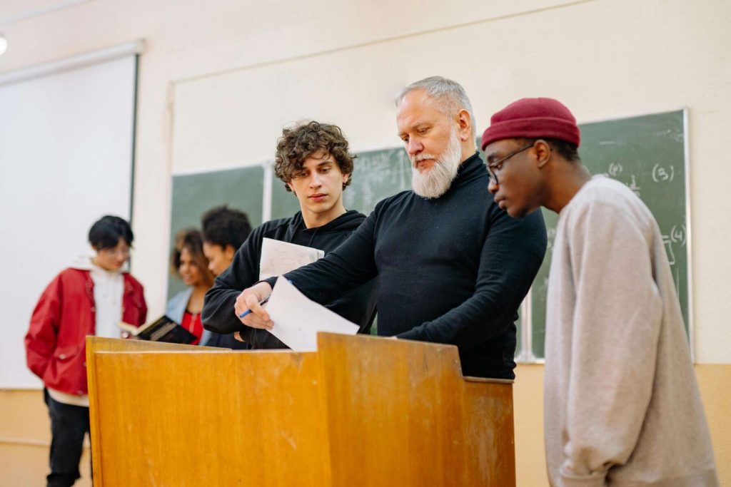 A teacher and students in the classroom are standing near a brown table