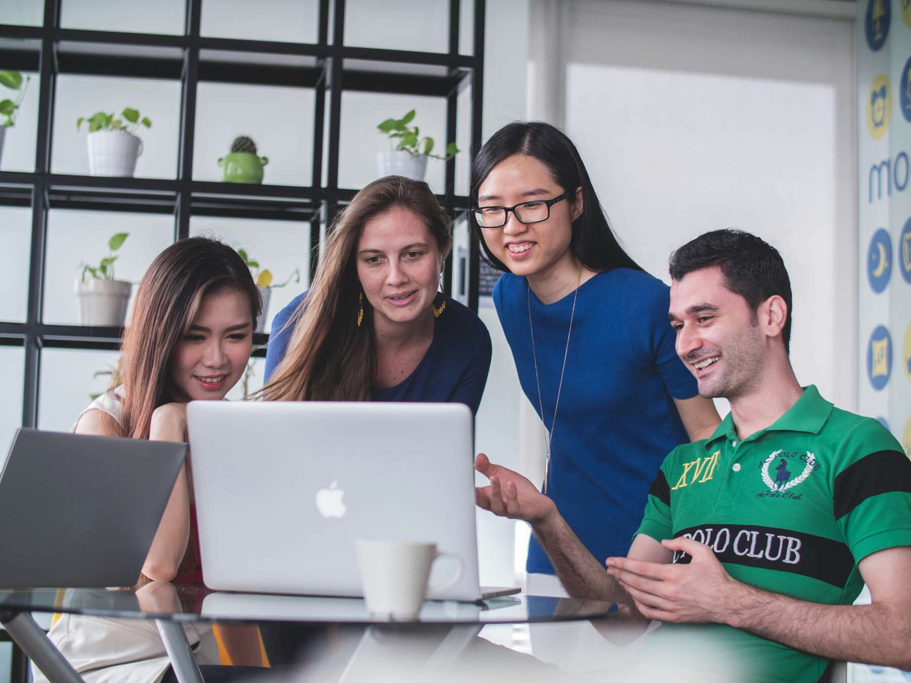 Four people looking at a white MacBook on top of a glass table