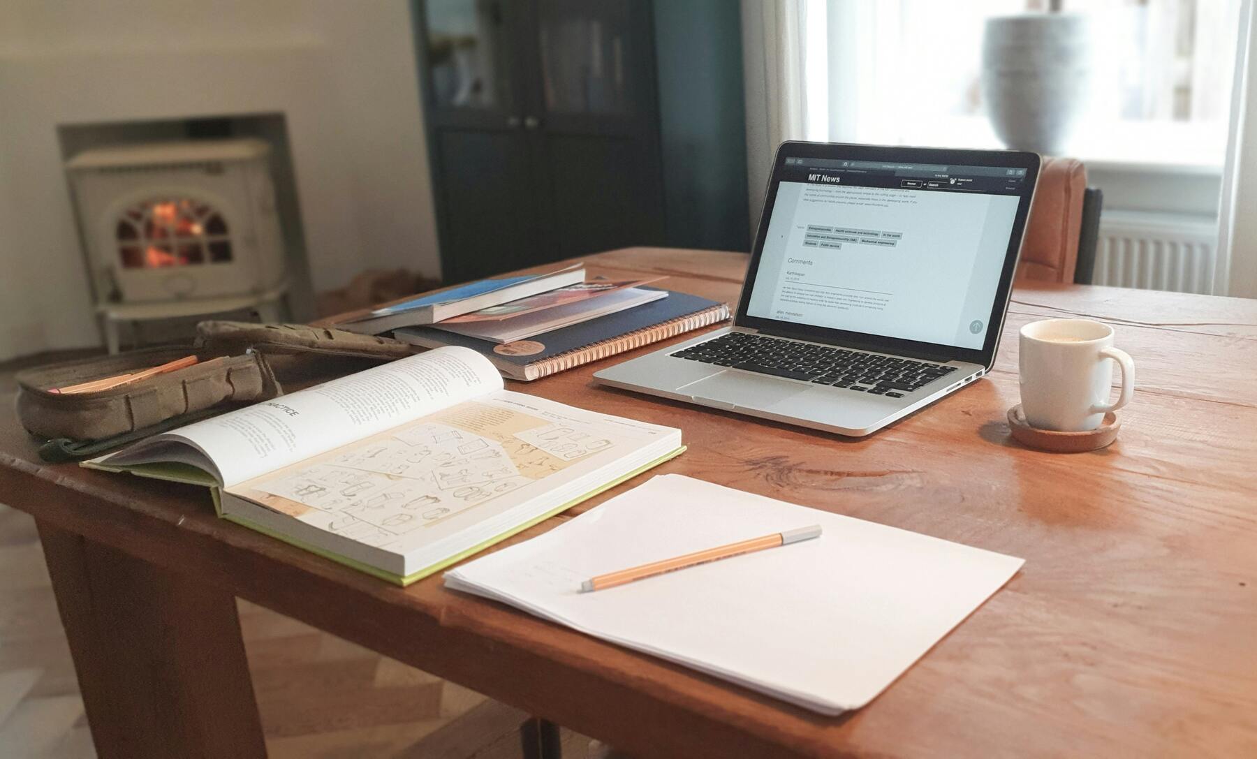 Notebooks, textbook, coffee mug and a running laptop all laid out on a table