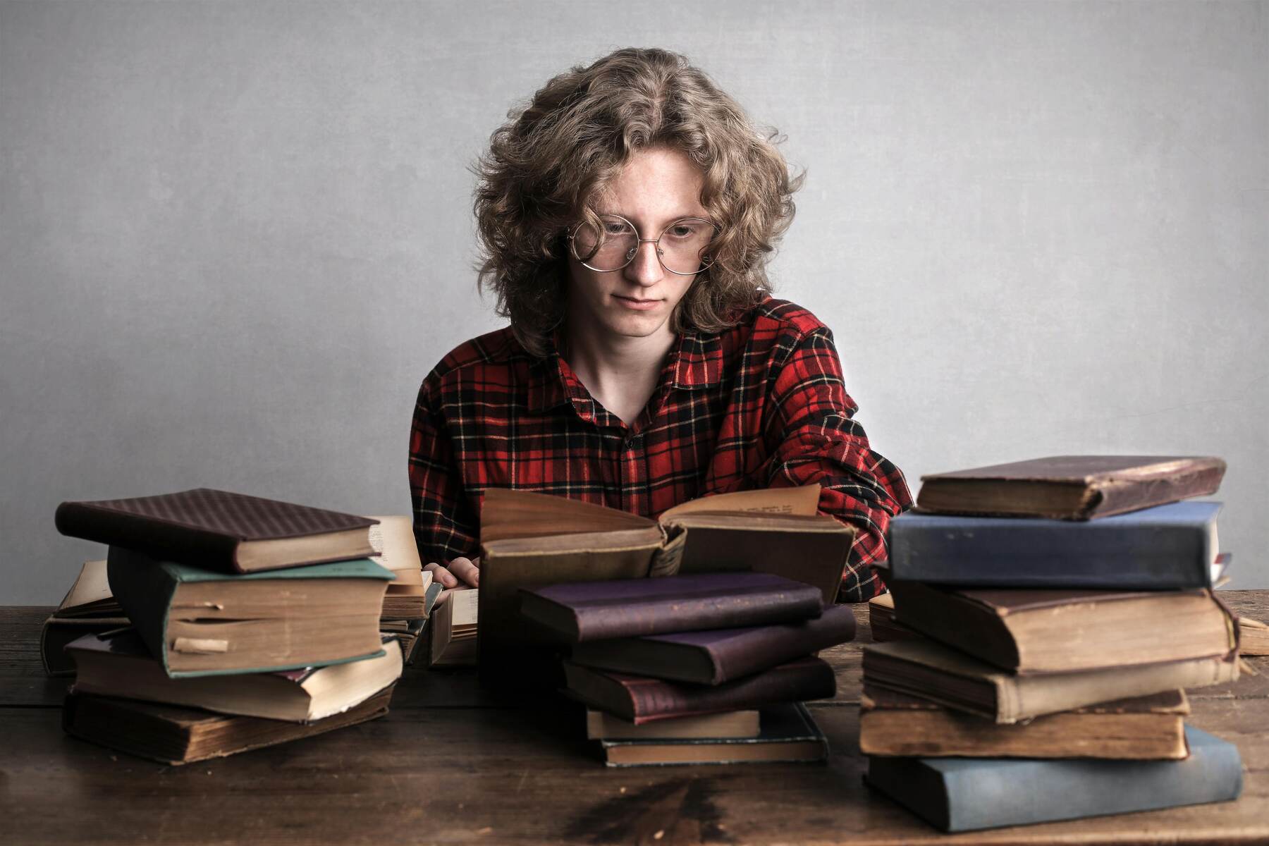 Man reading a book on top of a pile of books on the table
