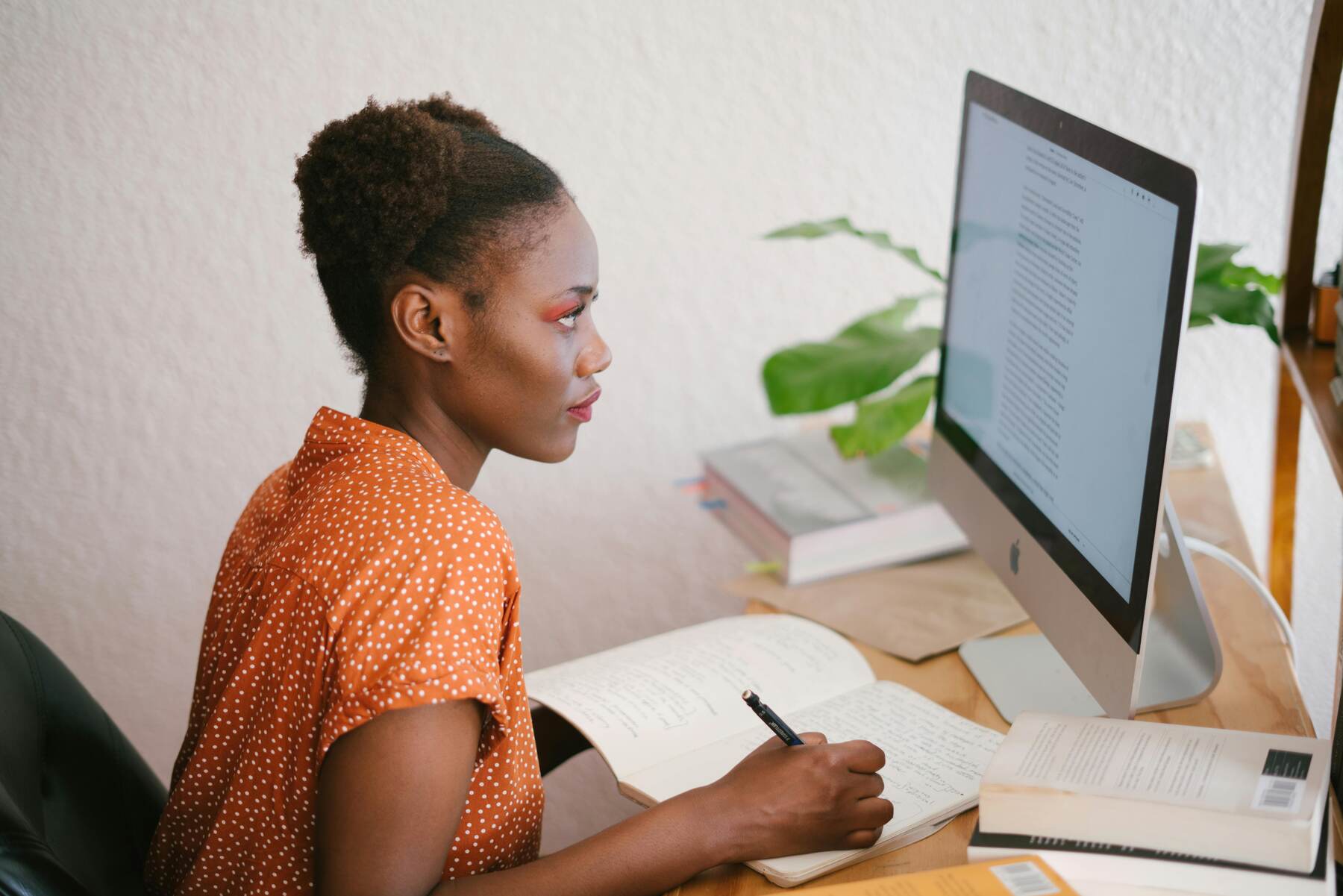Woman writing notes as she looks into her desktop monitor