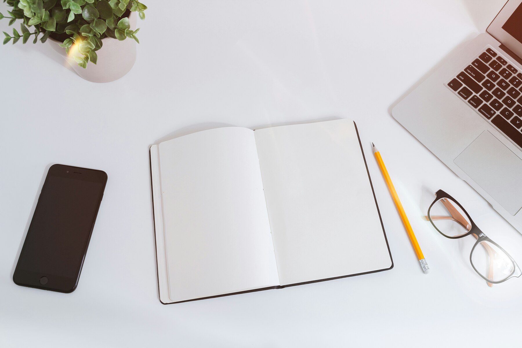 Opened notebook, smartphone, pencil, eyeglasses and laptop on a table