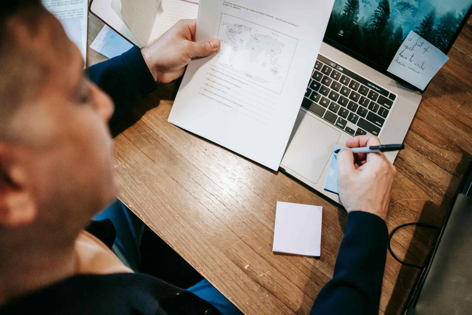 A man holding a pen and a paper with a note on his laptop