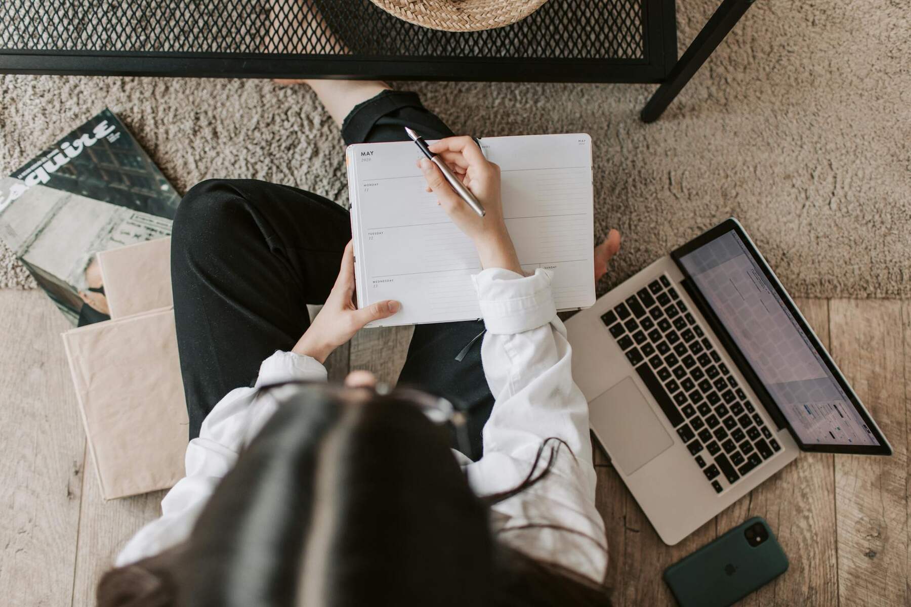 A woman sitting on the floor, writing on a notebook with a pen in her hand