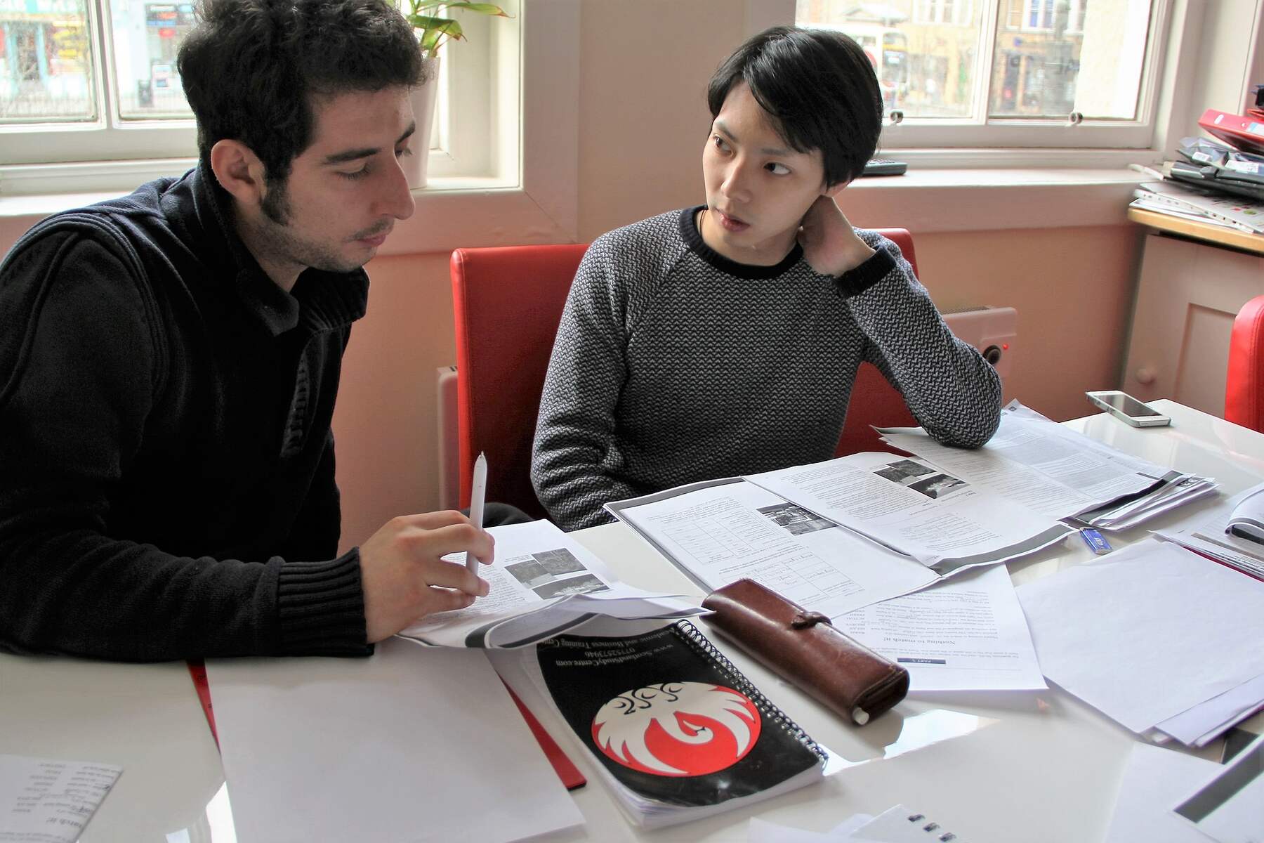 Two men sitting at a table with papers and discussing