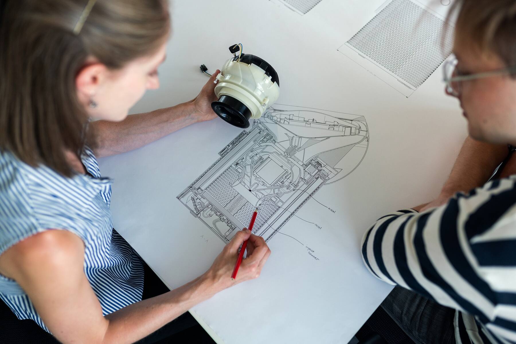 Two people studying a blueprint design on a table, discussing plans for a project