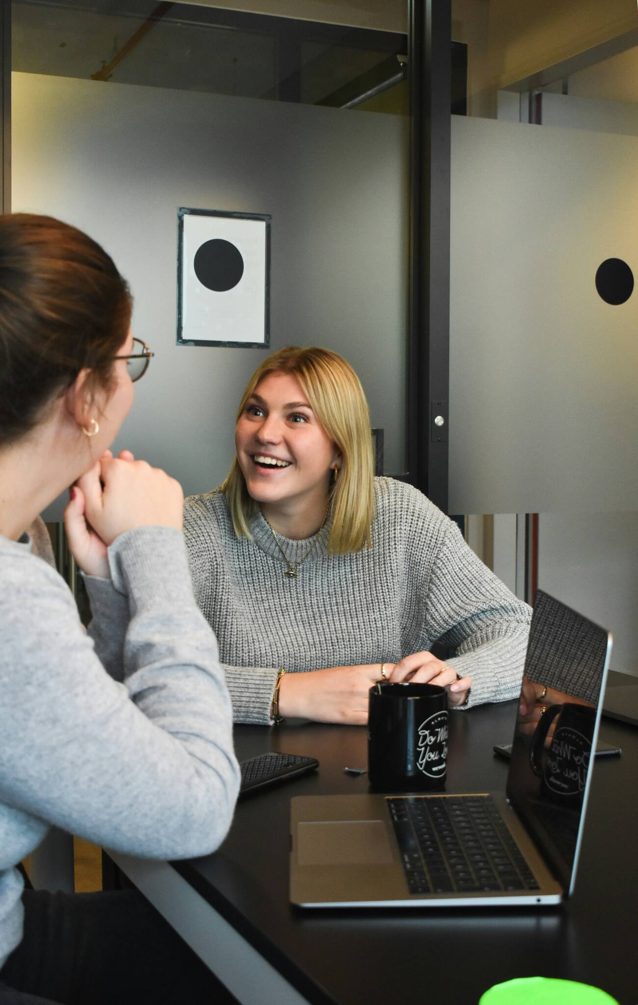 Two female professionals using laptops at a desk in a co-working space.