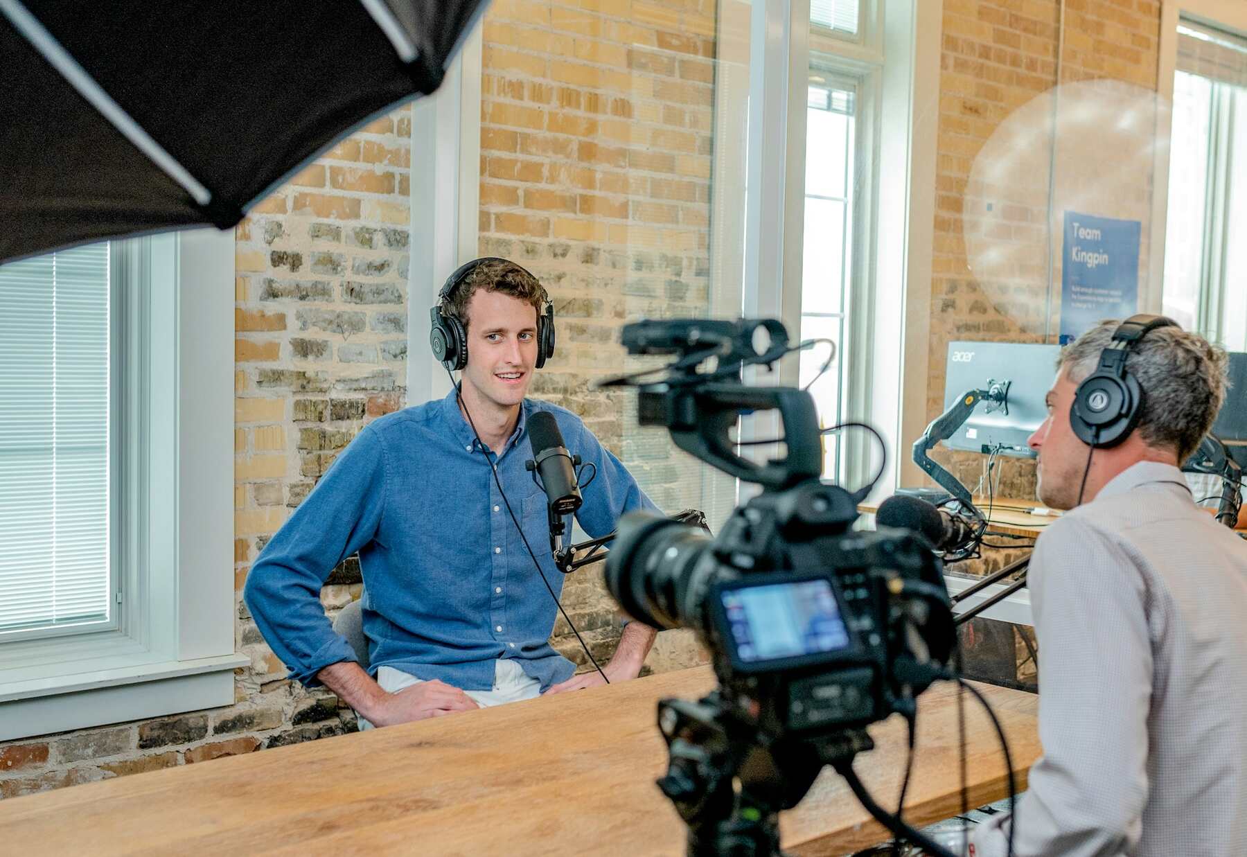 A man wearing a headphone with mic sitting in front of a camera at work