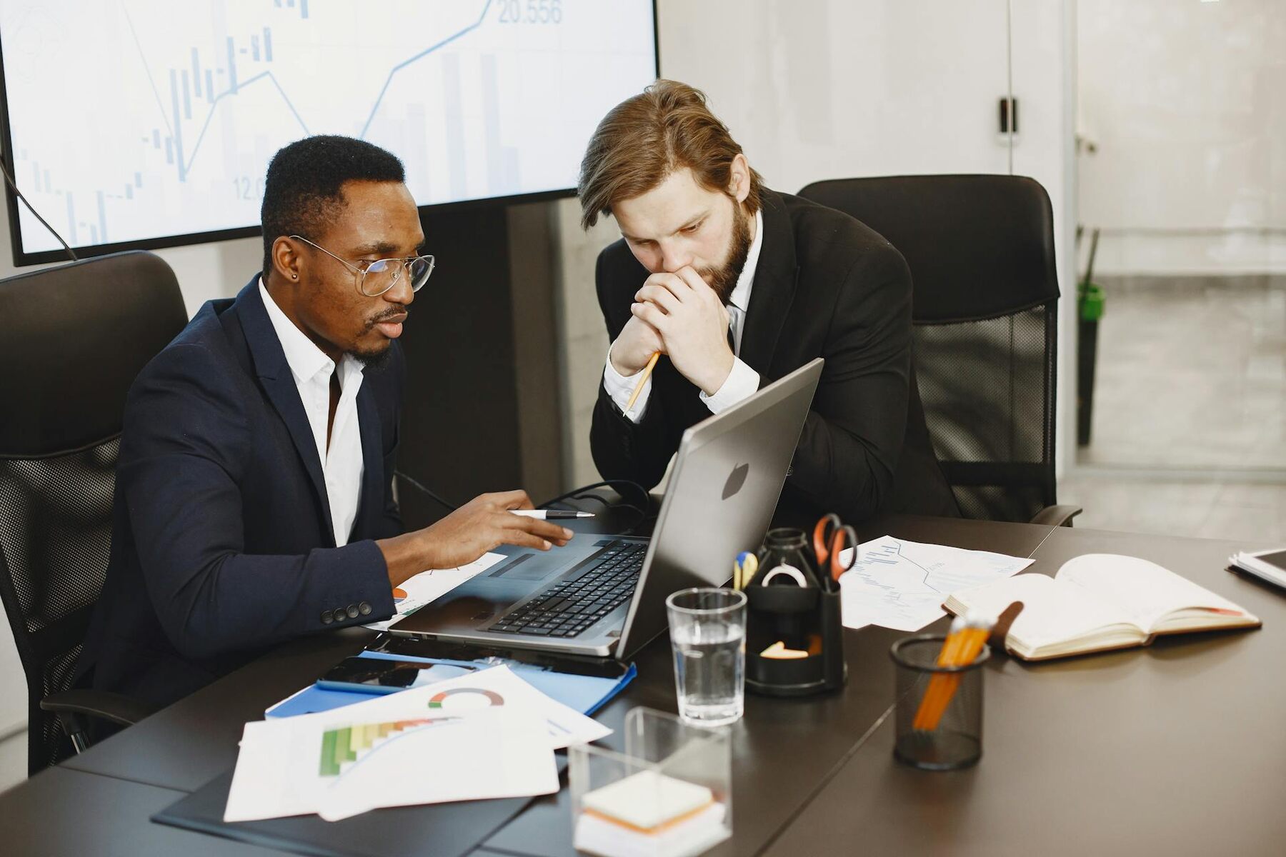 Two businessmen in suits sitting at a table, working on a laptop together