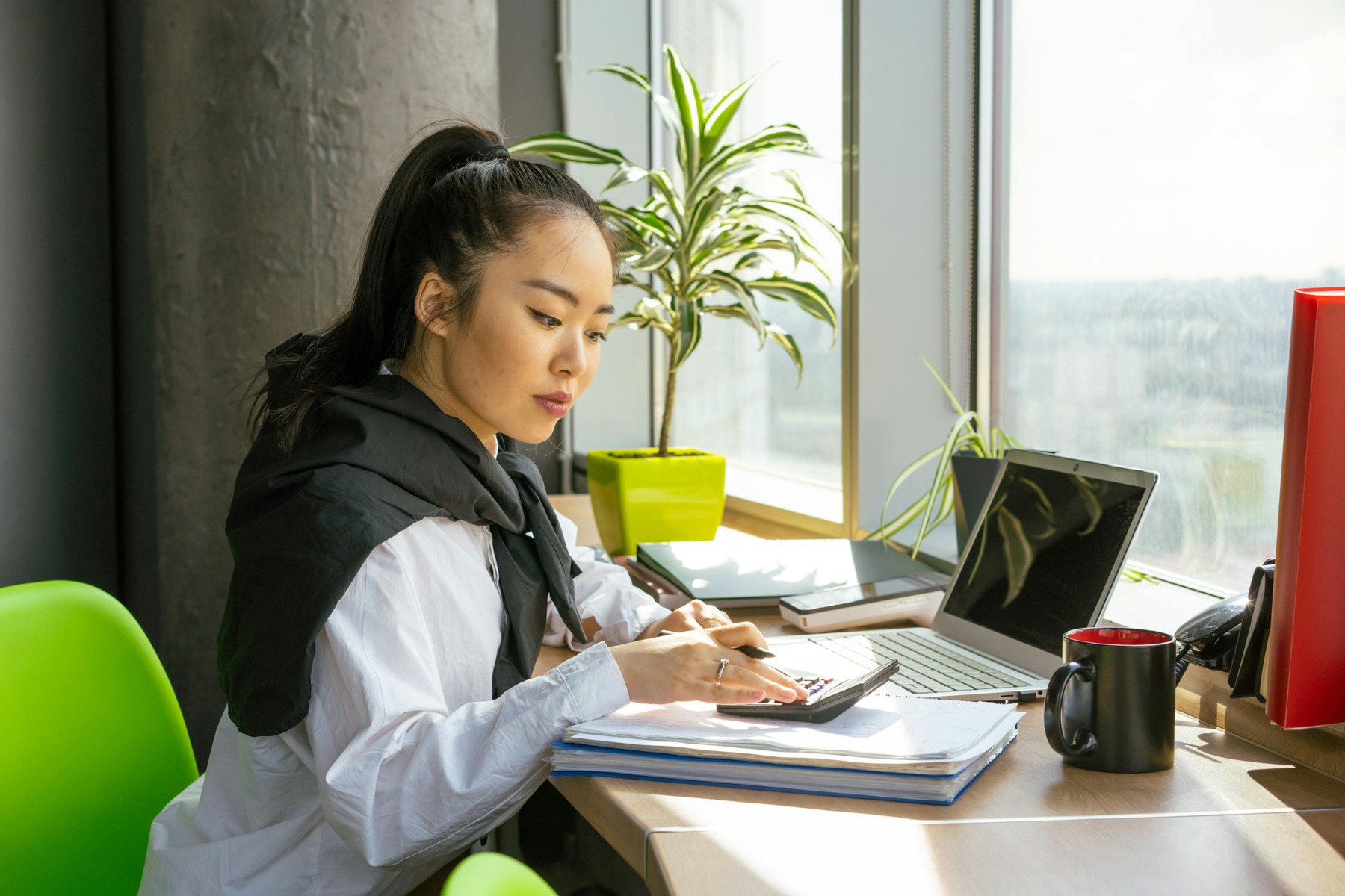 Woman using a calculator with her laptop in front of her