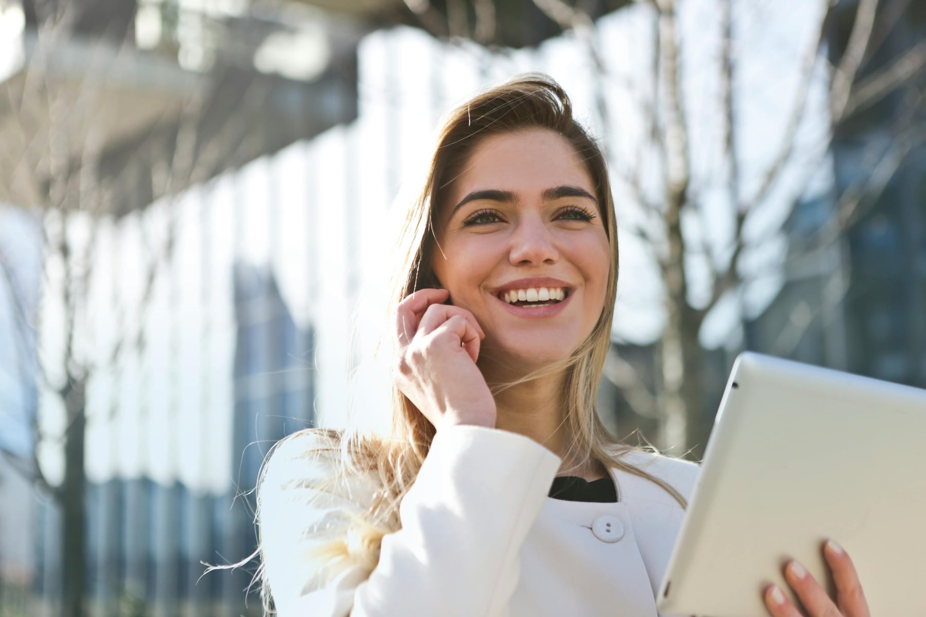 Woman smiling and holding a tablet, while answering a phone call outside